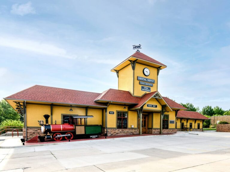 Exterior view of the Dental Depot dental office in Blue Springs, MO with model train, clock tower, and a yellow exterior.