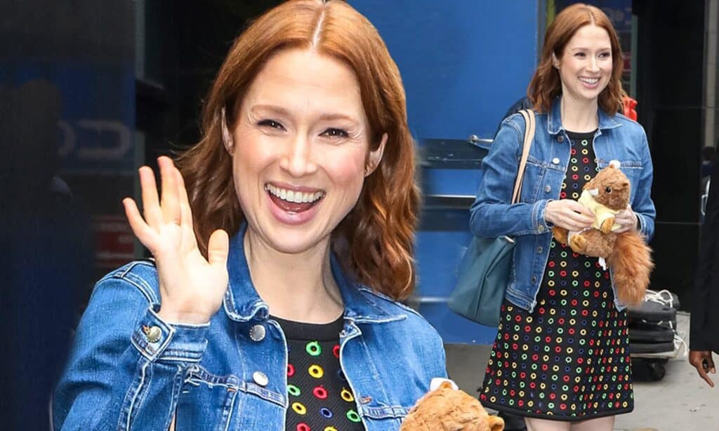 Ellie Kemper smiles for the camera and waves on the streets of NYC while holding a stuffed teddy bear.