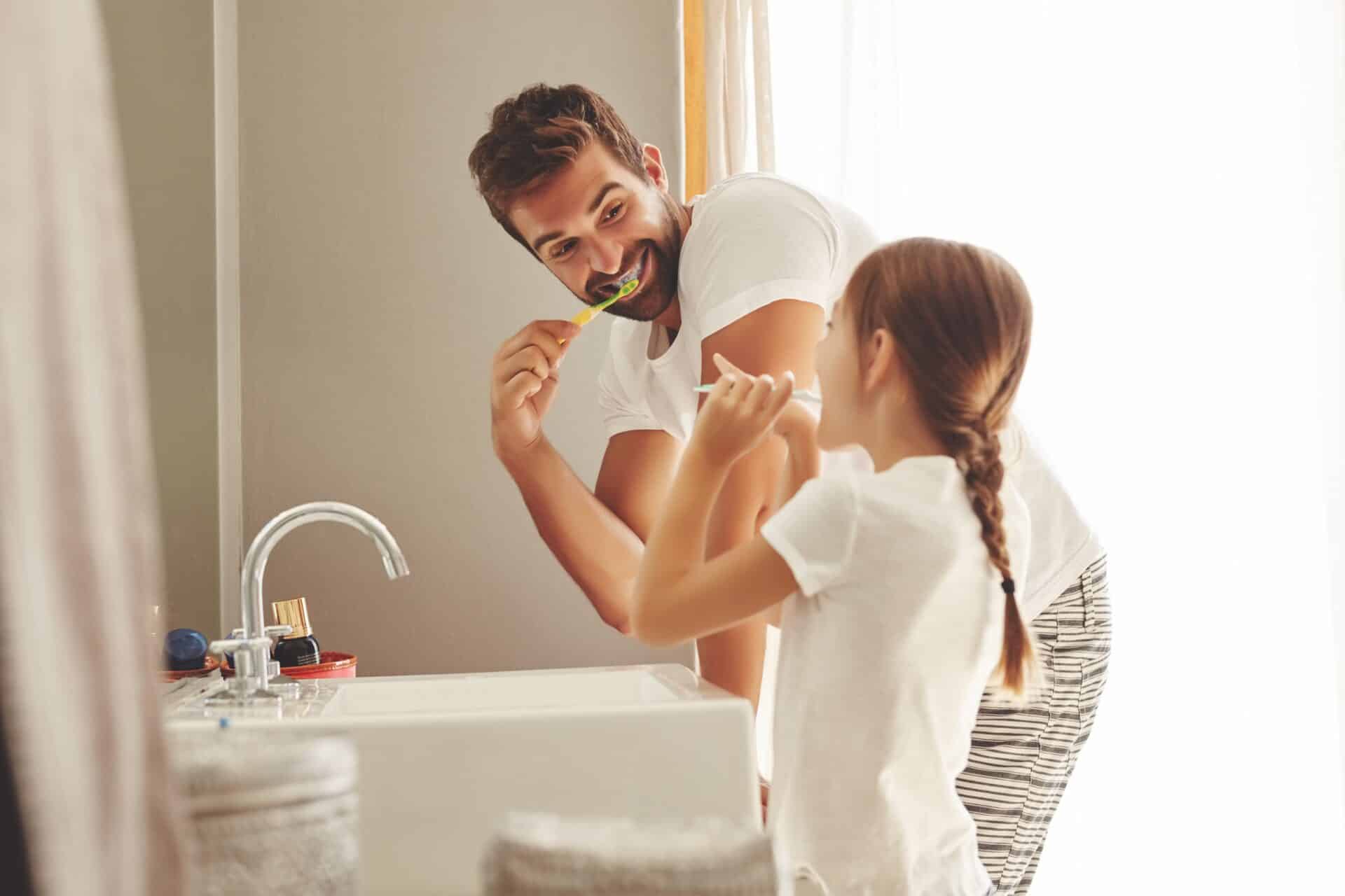 Dental care, father with daughter brush their teeth and in bathroom of their home.