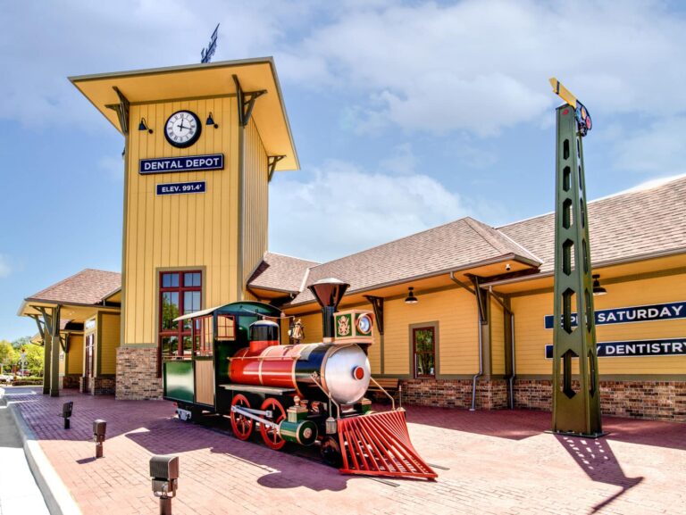 Exterior view of Dental Depot's dentist office with a model train in front, yellow walls, and a clock tower.