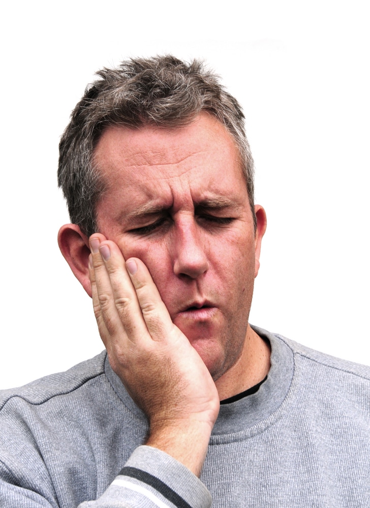 Middle aged man holds the side of his face due to a dental emergency