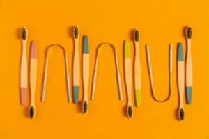 Various metal and bristled tongue brushes lay out, perfectly spaced in front of a goldenrod background.