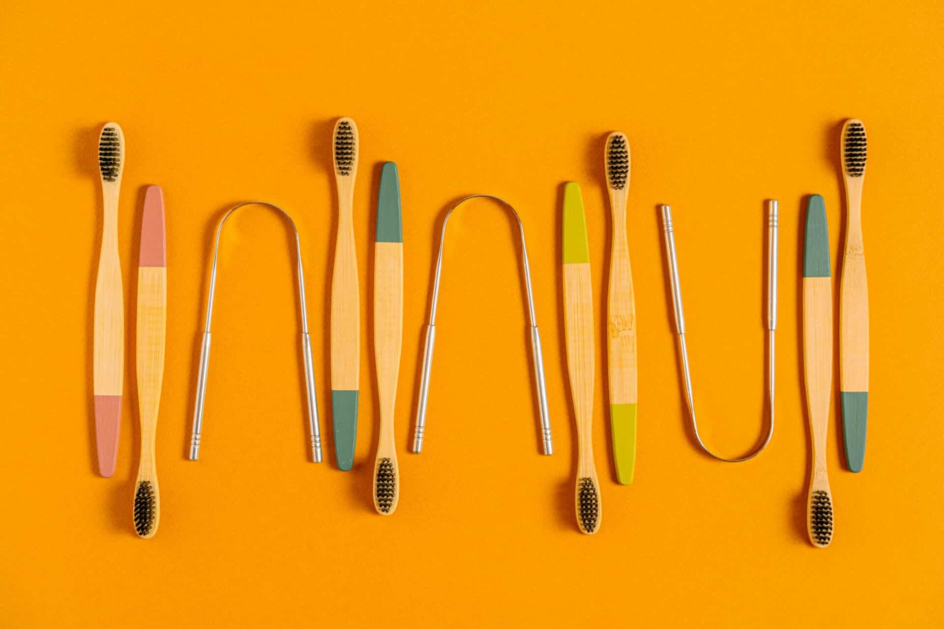 Various metal and bristled tongue brushes lay out, perfectly spaced in front of a goldenrod background.
